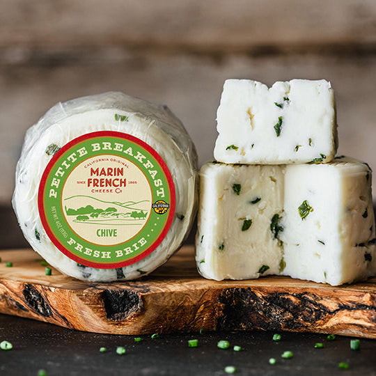 Marin French cheese with a round container and sliced pieces on a wooden board.